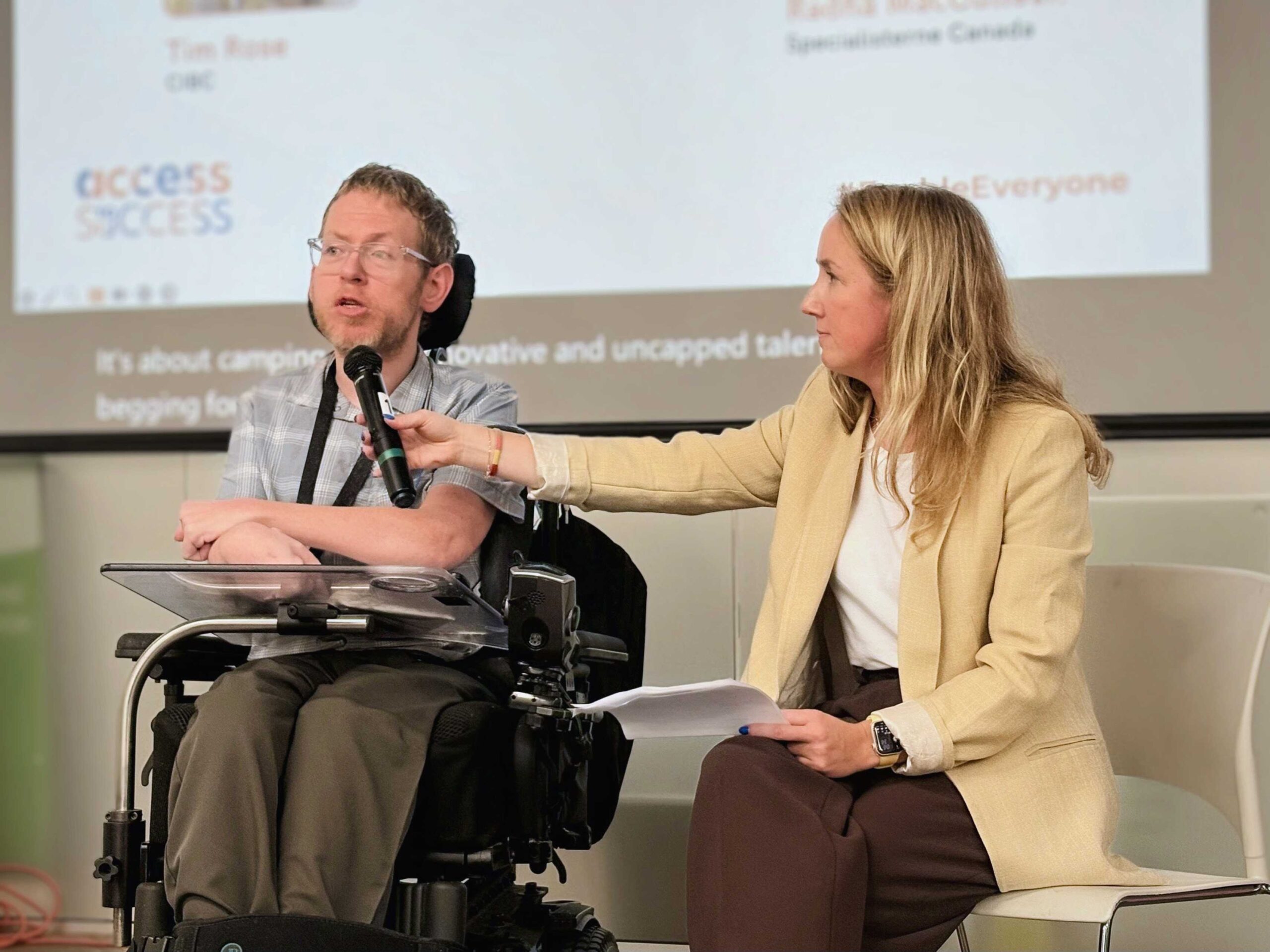 A woman is holding a microphone for a man in a wheelchair during his speech